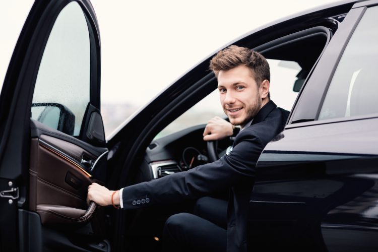 Confident Chauffeur. Guy in suit sitting in driver's seat, getting in his car at downtown area, closing the door